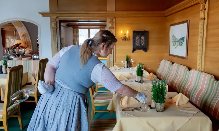 Mitarbeiterin deckt in einer hellen Gaststube einen Tisch ein